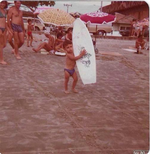 Edu aos dois anos na praia, segurando uma prancha de surf